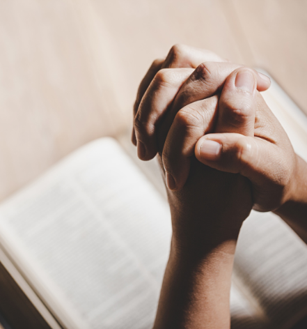 Hands clasped in prayer over an open Bible